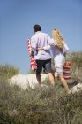 Rear view of embracing couple walking on beach with bag and beach umbrella — Stock Photo