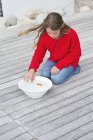 Girl touching red fish in bowl on wooden pier — Stock Photo