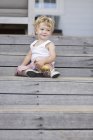 Niedlicher kleiner Junge sitzt auf Holzstufen mit Spielzeug — Stockfoto