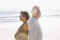 Nachdenkliches Senioren-Paar steht Rücken an Rücken sonnig am Strand — Stockfoto
