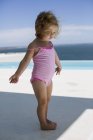 Gros plan de bébé fille en maillot de bain rose marchant près de la piscine — Photo de stock
