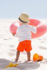 Rückansicht eines Jungen, der am Strand mit einem aufblasbaren Ring spielt — Stockfoto