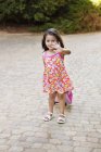 Petite fille en robe d'été portant des bagages et agitant la main à l'extérieur — Photo de stock