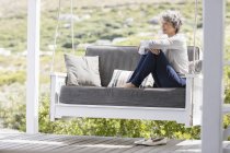 Heureuse femme mature assise sur la balançoire dans le porche — Photo de stock