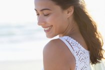 Lächelnde junge Frau mit geschlossenen Augen am Strand im Sonnenlicht — Stockfoto