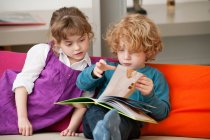 Junge sitzt mit seiner Schwester und liest ein Buch — Stockfoto