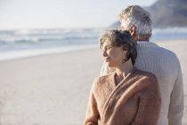 Close-up of relaxed thoughtful senior couple standing back to back on beach — Stock Photo