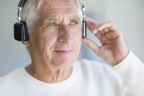 Hombre mayor escuchando música con auriculares y mirando hacia otro lado - foto de stock