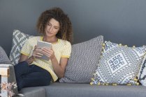 Жінка сидить на дивані вдома і використовує цифровий планшет — стокове фото
