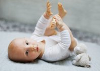 8 mois bébé garçon couché et jouer avec ses pieds — Photo de stock