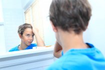 Francia, giovane ragazzo in bagno che guarda i capelli allo specchio. — Foto stock