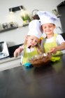 Deux jeunes enfants heureux enfants garçon et fille famille avec tablier et chapeau de chef préparer des biscuits drôles dans la cuisine à la maison. — Photo de stock