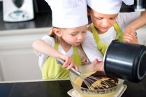 Deux jeunes enfants heureux enfants garçon et fille famille avec tablier et chapeau de chef préparer des biscuits drôles dans la cuisine à la maison. — Photo de stock