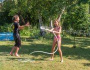 Due ragazzi di 4 anni e 12 anni e una bambina di 10 anni che gioca con un tubo in giardino — Foto stock