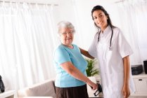 Cheerful young rehab nurse helping elderly senior woman using a walker — Stock Photo