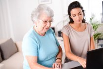 Cheerful young woman helping an elderly senior person using laptop  computer for internet search and email — Stock Photo