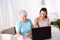 Веселая молодая женщина помогает пожилой пожилой человек, используя ноутбук для поиска в Интернете и электронной почты — стоковое фото
