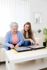 Elderly woman with her young granddaughter at home looking at memory in family photo album — Stock Photo