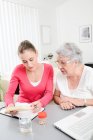 Cheerful young woman helping elderly woman with pills medical prescription — Stock Photo