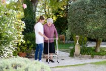 Anziana donna anziana con un'infermiera che cammina all'aperto nel giardino dell'ospedale della casa di cura — Foto stock
