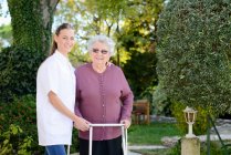 Пожилая пожилая женщина с медсестрой, гуляющей на открытом воздухе в саду больницы — стоковое фото