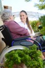Anciana mujer mayor en silla de ruedas con una enfermera al aire libre en casa de ancianos hospital jardín. - foto de stock