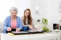 Elderly woman with her young granddaughter at home looking at memory in family photo album — Stock Photo