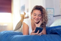 Menina adolescente e vida cotidiana. Na cama com smartphone — Fotografia de Stock