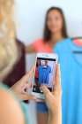 Adolescente joven en casa con un teléfono inteligente utilizando la aplicación Vinted para vender su ropa - foto de stock