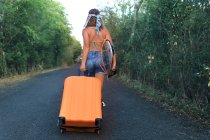 Une fille avec une valise. Jeune et jolie hippie sur une route déserte — Photo de stock