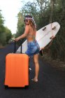 Une fille avec une valise. Jeune et jolie hippie sur une route déserte — Photo de stock