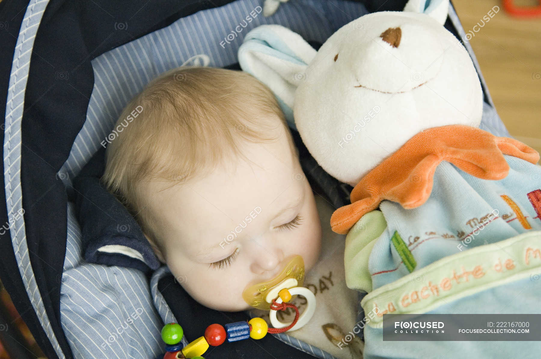 Baby girl sleeping in baby carrier with stuffed toy — eyes closed