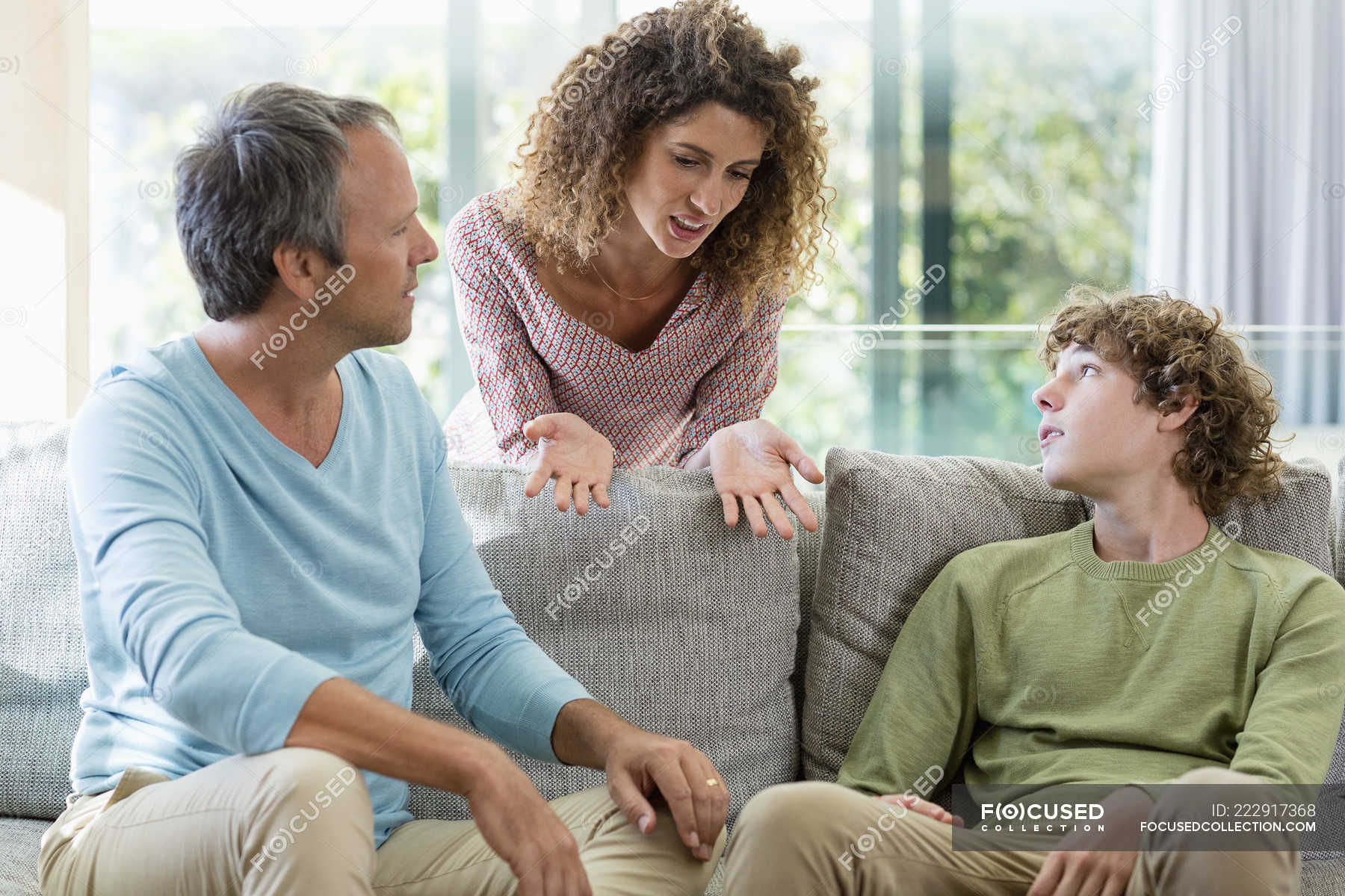 Happy family talking on sofa in living room at home — male, indoors ...