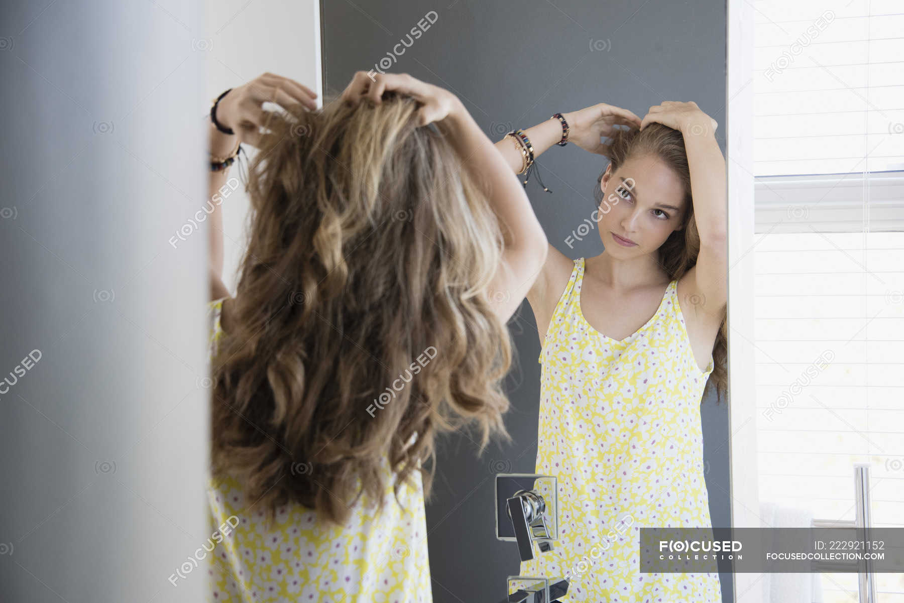 Teenage girl examining hair in mirror — lock of hair, indoors - Stock Photo  | #222921152