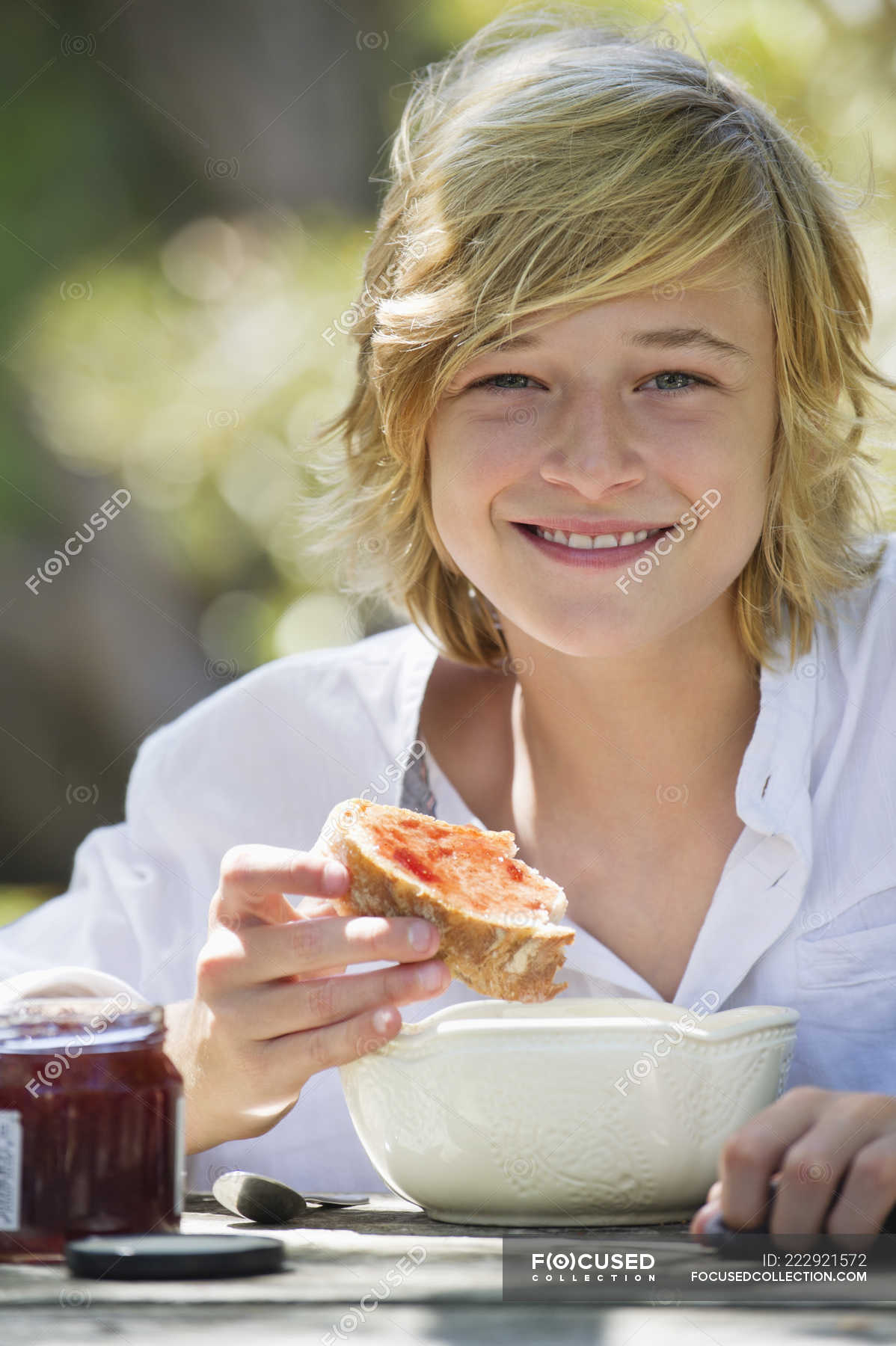 Portrait of teenage boy eating bread with jam outdoors — sitting ...