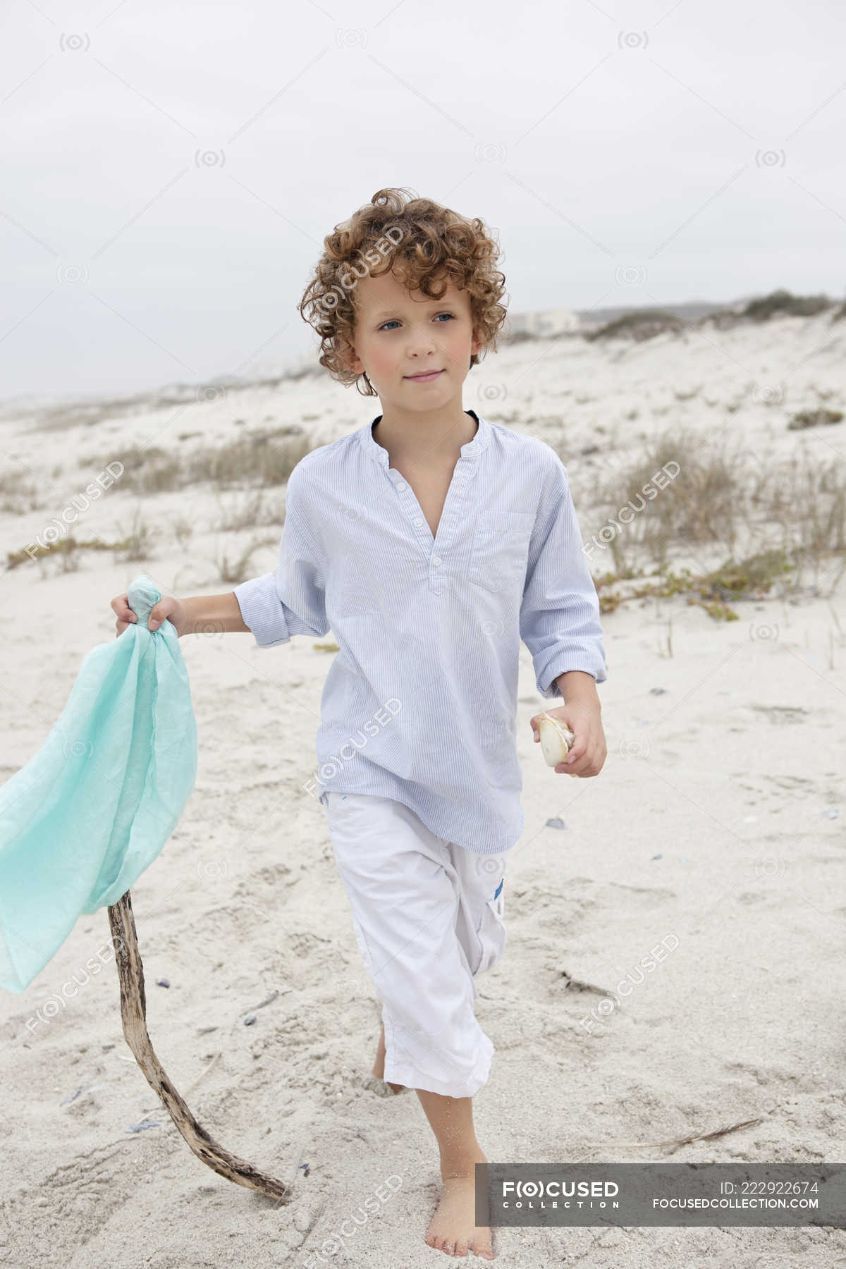 Boy holding flag on stick and walking on sandy beach — looking away ...