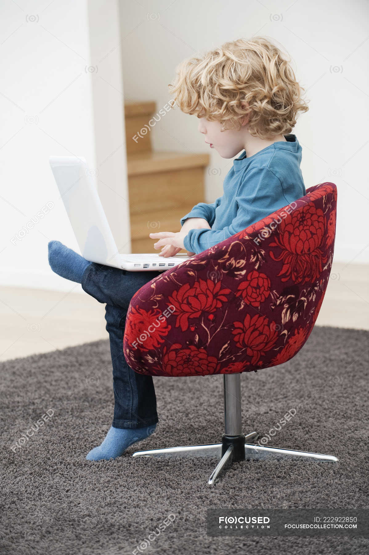 Cute Boy With Blonde Hair Using A Laptop In Armchair At Home