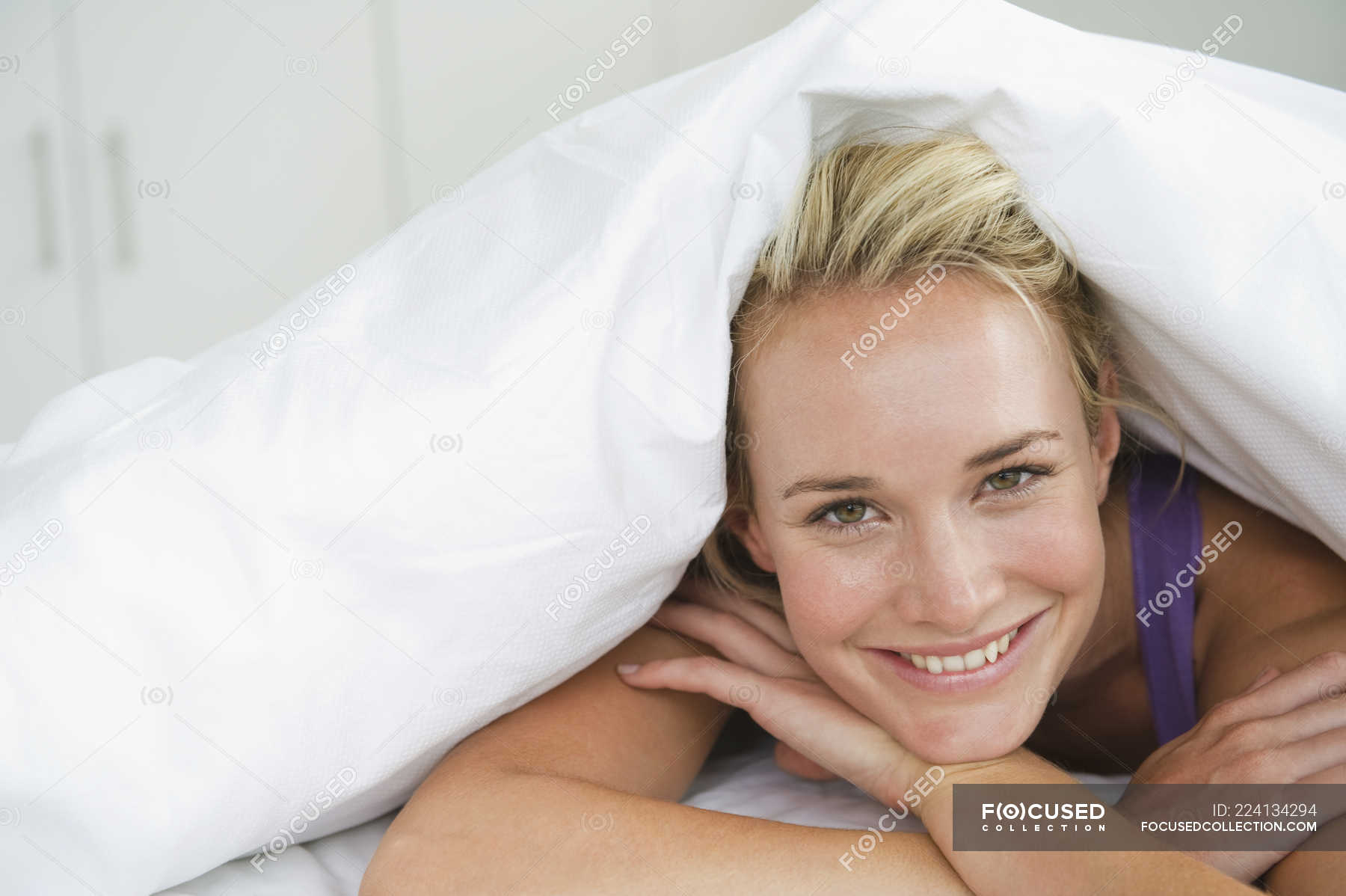 Closeup of woman lying on bed under duvet and smiling — covering