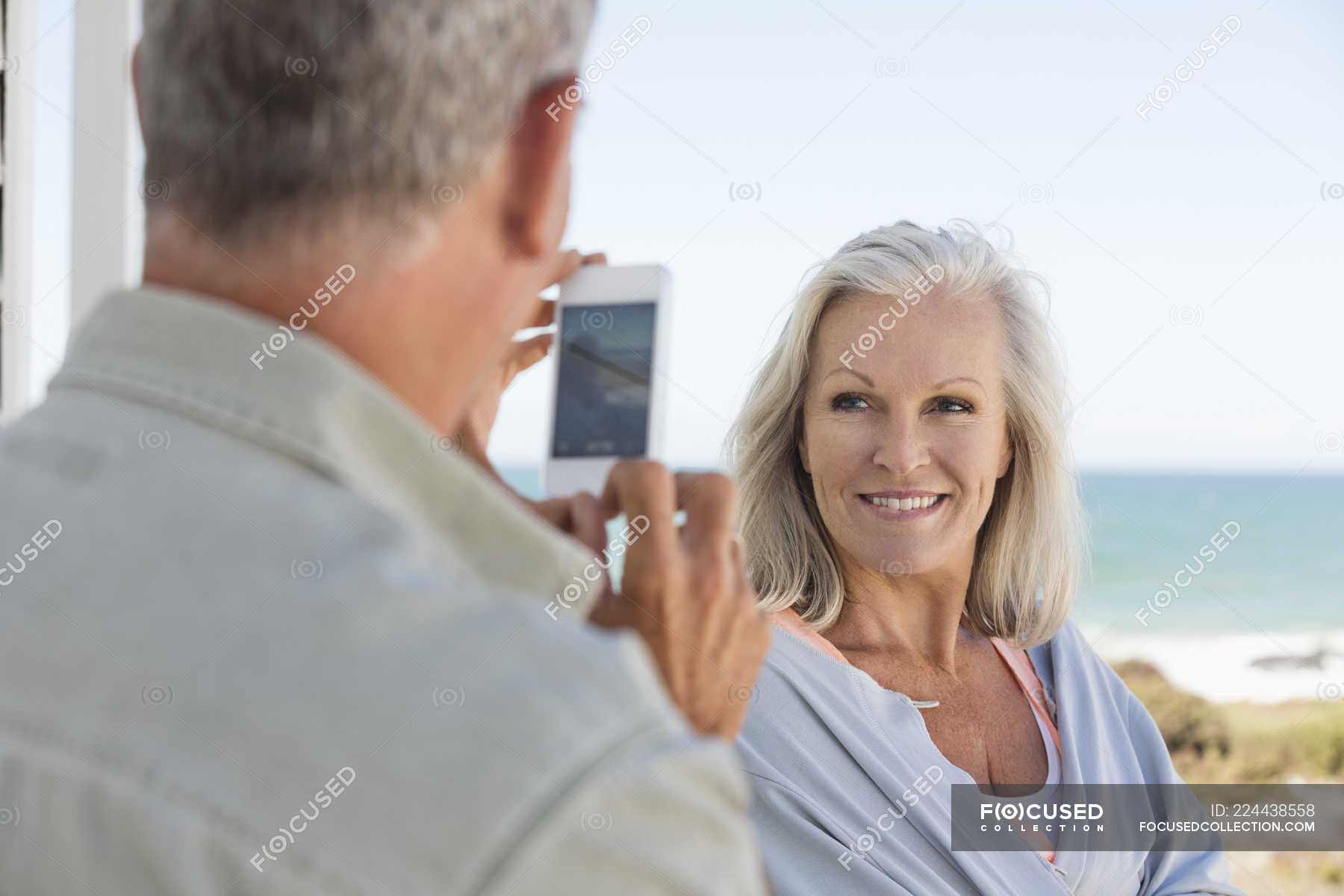 Mann fotografiert Ehefrau mit Handy am Strand — im Freien, Kamera