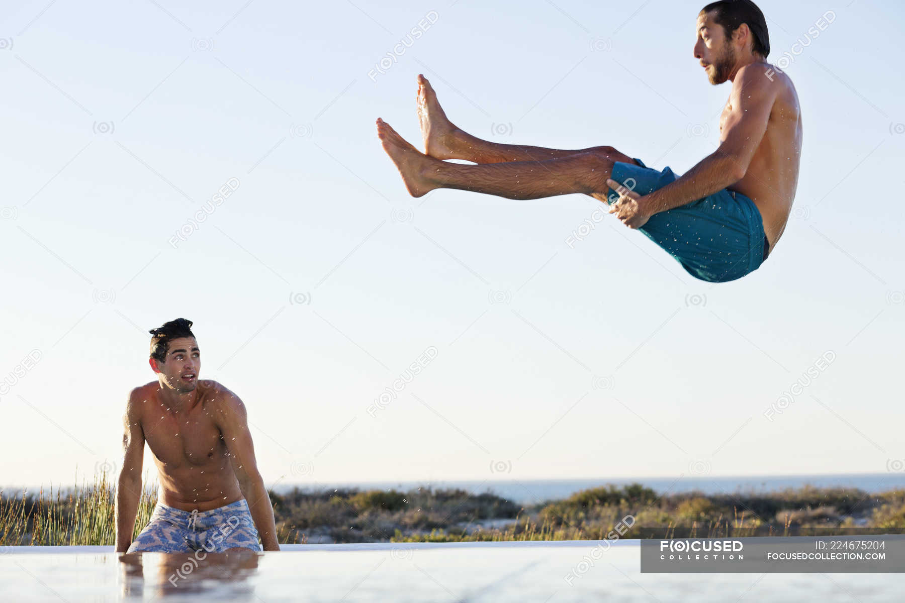 Man jumping into swimming pool with friend standing at poolside — Men