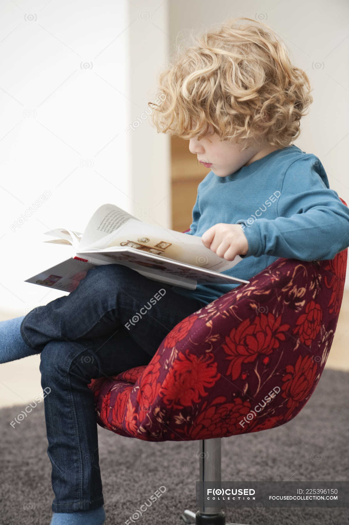 Cute Boy With Blonde Hair Reading A Book In Armchair At Home