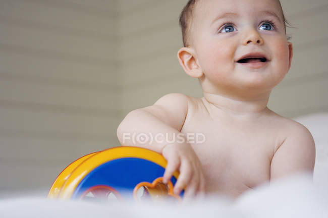 Nu bébé garçon jouer assis sur le lit et jouer avec jouet — Photo de stock