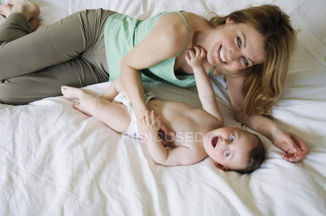 Glückliche Mutter und Baby liegen auf dem Bett und schauen in die Kamera — Stockfoto