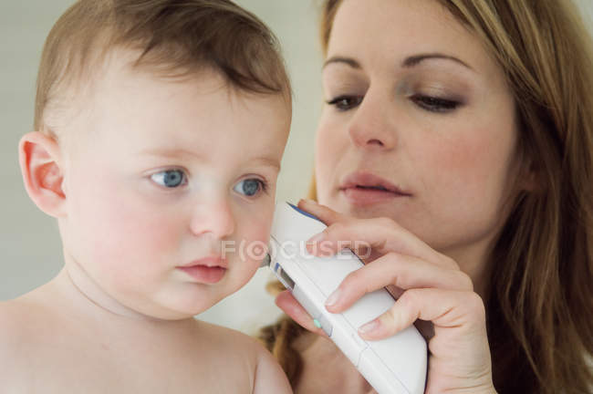 Mother taking baby temperature with ear-thermometer — Stock Photo