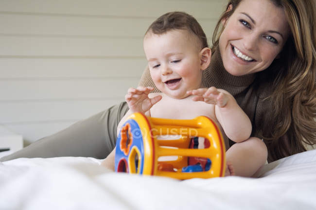 Mother and naked baby playing while sitting on bed — Stock Photo