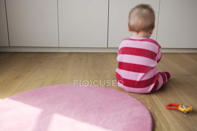 Visão traseira do menino em pijama listrado sentado no chão e brincando — Fotografia de Stock