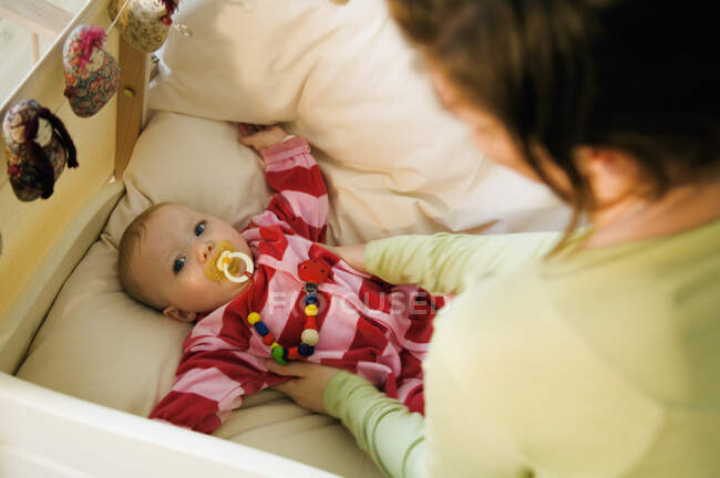 Madre poniendo a su bebé en la cama, edredón - foto de stock