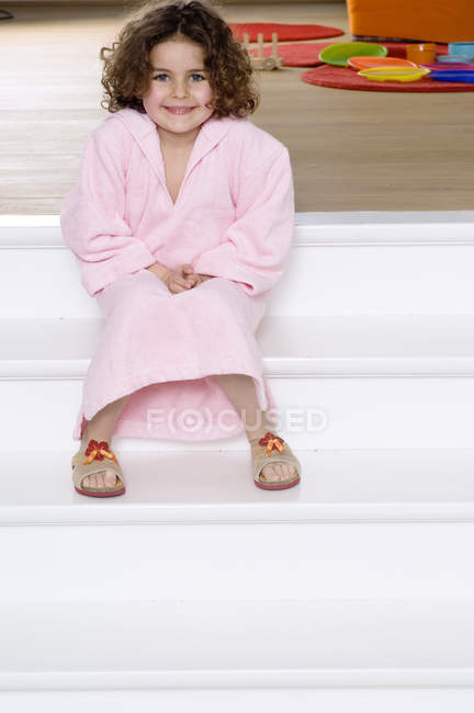 Little girl in bathrobe sitting on stairs and smiling — Stock Photo