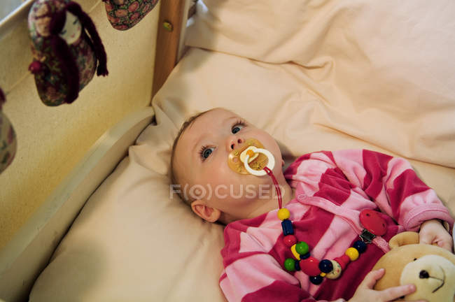 Bebê menina deitada na cama com consolador — Fotografia de Stock
