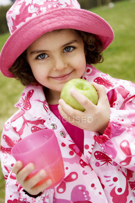 Portrait de petite fille tenant pomme et verre à l'extérieur — Photo de stock